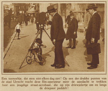 871823 Afbeelding van een jongetje op een driewieler, die onder een driepoot van een filmcamera door fietst, ...